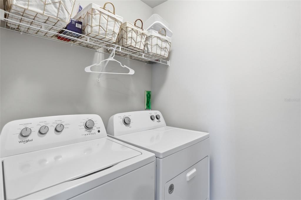 A laundry room features a white washer and dryer beneath a wire storage shelf — 8909 CASCADE PRICE CIRCLE, NORTH FORT MYERS, FL