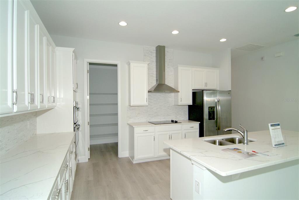 A modern kitchen features white cabinets, quartz countertops, stainless steel appliances, and a center island — 9582 RODBELL STREET, ORLANDO, FL