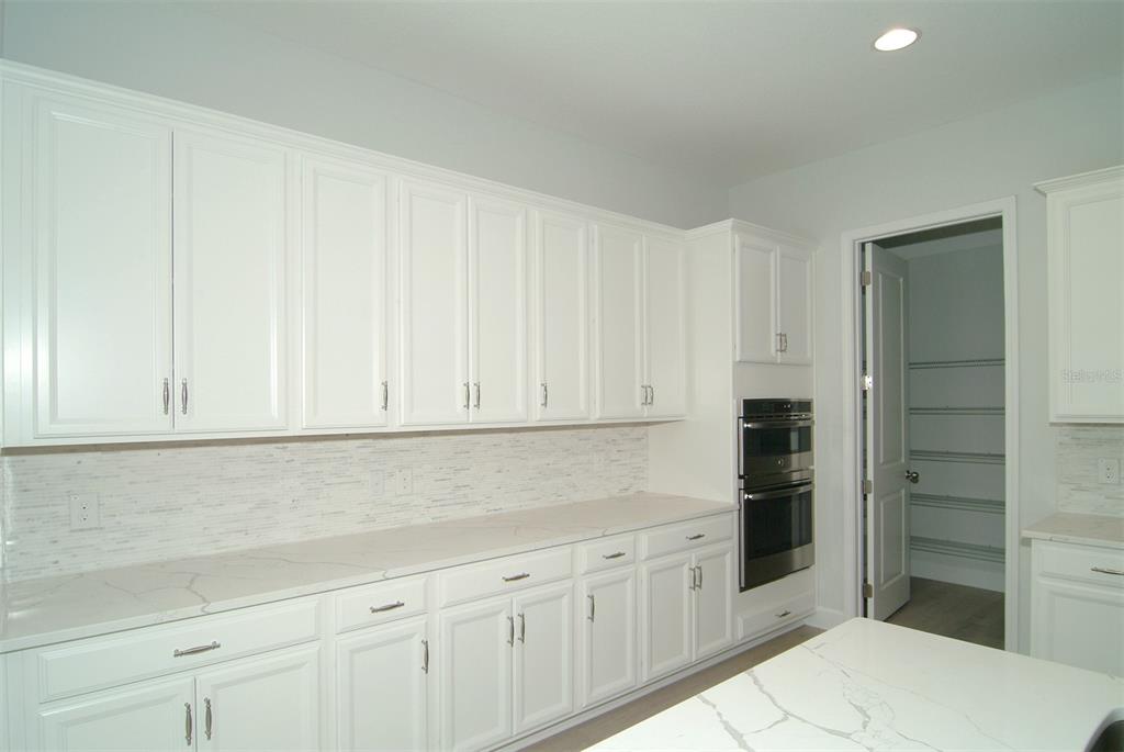 A kitchen features white cabinets, marble-look countertops, a tiled backsplash, and a double wall oven — 9582 RODBELL STREET, ORLANDO, FL
