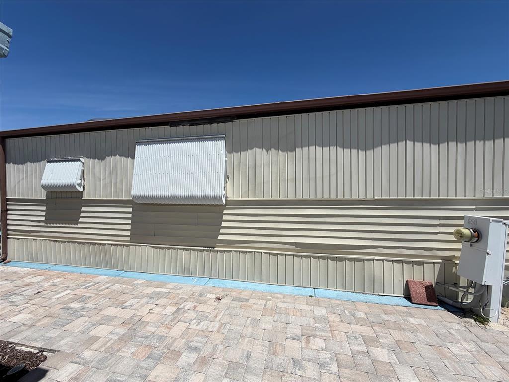 The exterior of a mobile home features light-colored metal siding, two window awnings, and pavers — 9000 US HIGHWAY 192 UNIT 650, CLERMONT, FL