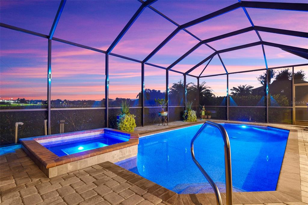 A screened-in swimming pool and hot tub area at sunset with stone paver decking — 20203 GRANLAGO DRIVE, VENICE, FL