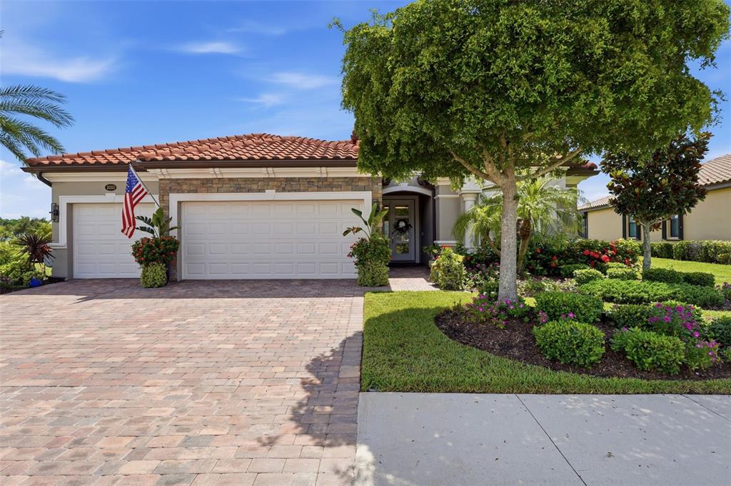 A single-story house with a tiled roof, stone facade, and a paved driveway — 20203 GRANLAGO DRIVE, VENICE, FL