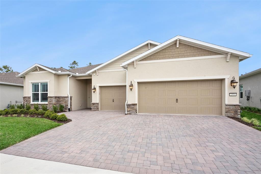 A single-story house with a beige stucco exterior, stone accents, and a three-car garage — 2555 PINE PRESERVE COURT, ST CLOUD, FL