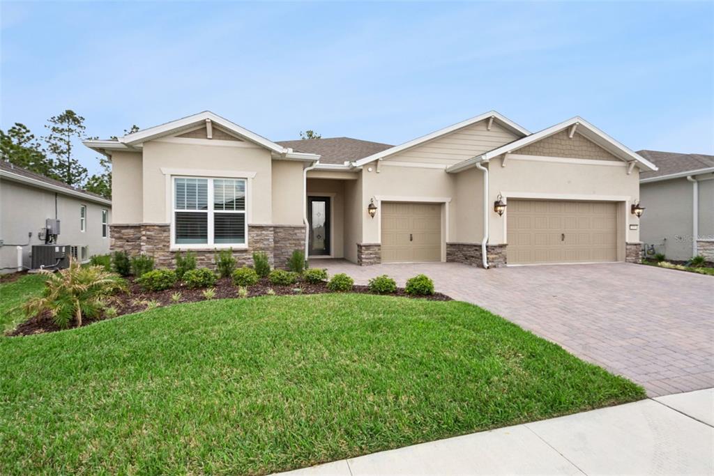 A single-story house with a beige stucco exterior, stone accents, and a three-car garage — 2555 PINE PRESERVE COURT, ST CLOUD, FL