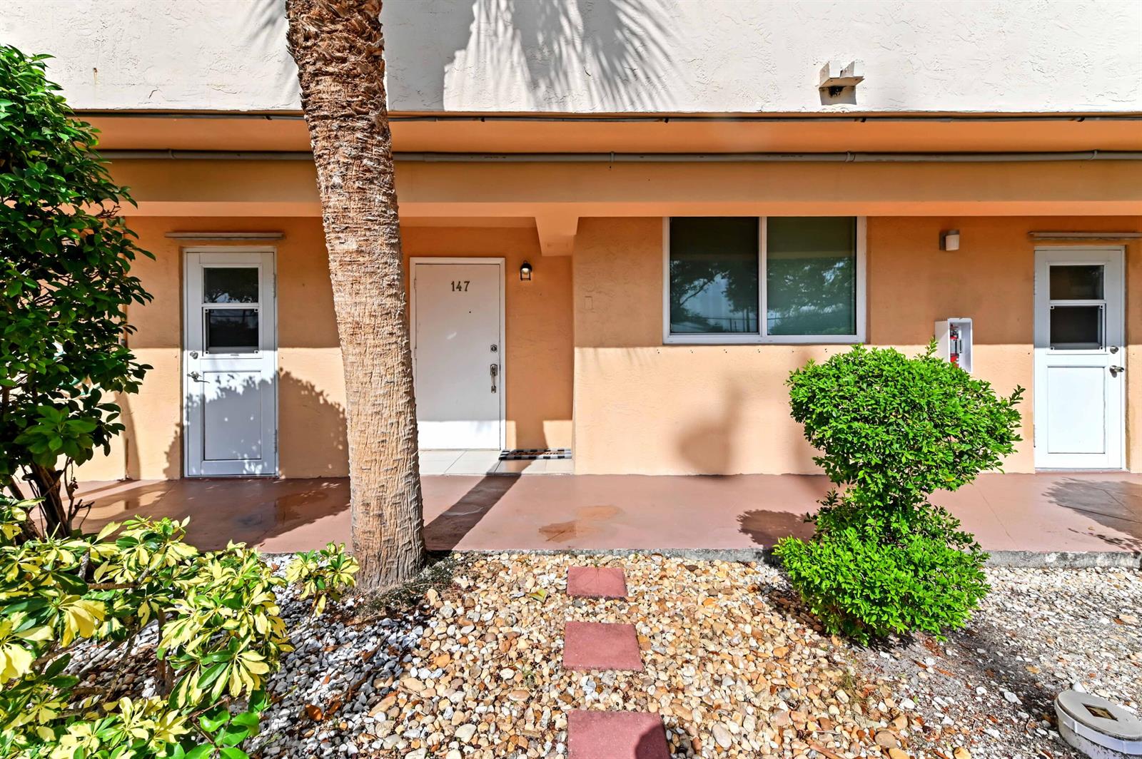 The exterior of a peach-colored building features a walkway, a palm tree, and unit 147 — 4500 N Federal Highway # 147f, Lighthouse Point FL 33064, LIGHTHOUSE POINT, FL