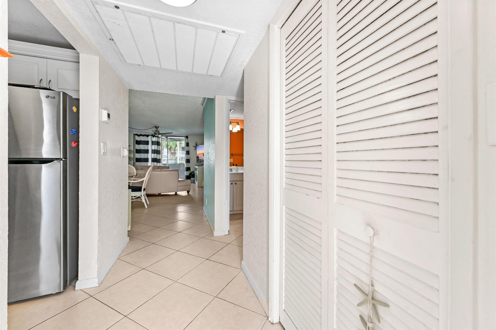 A hallway with tile flooring leads to a living area, featuring a louvered closet door — 4500 N Federal Highway # 147f, Lighthouse Point FL 33064, LIGHTHOUSE POINT, FL