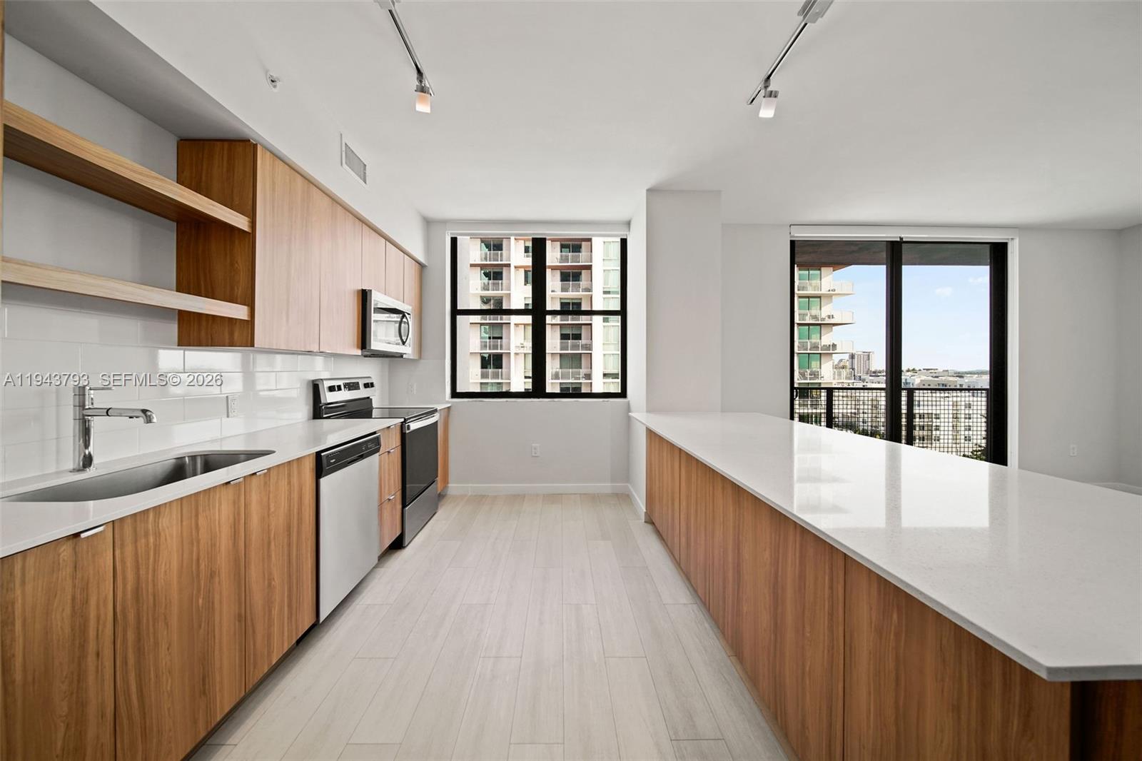 A modern kitchen features light wood cabinetry, white countertops, stainless steel appliances, and large windows — FORT LAUDERDALE, FL