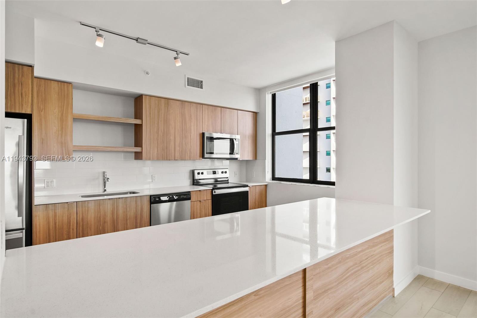 A modern kitchen features wood-toned cabinetry, white countertops, stainless steel appliances, and a large island — FORT LAUDERDALE, FL