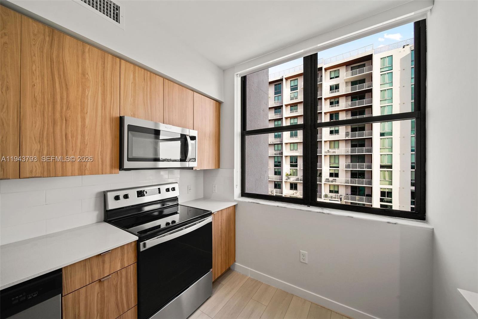 A modern kitchen features light wood cabinets, stainless steel appliances, and a large window view — FORT LAUDERDALE, FL