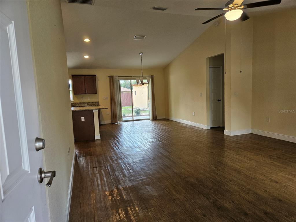 An open-concept living area features wood-look flooring, a vaulted ceiling, and an adjacent kitchen — 11 ALMOND TRAIL, OCALA, FL