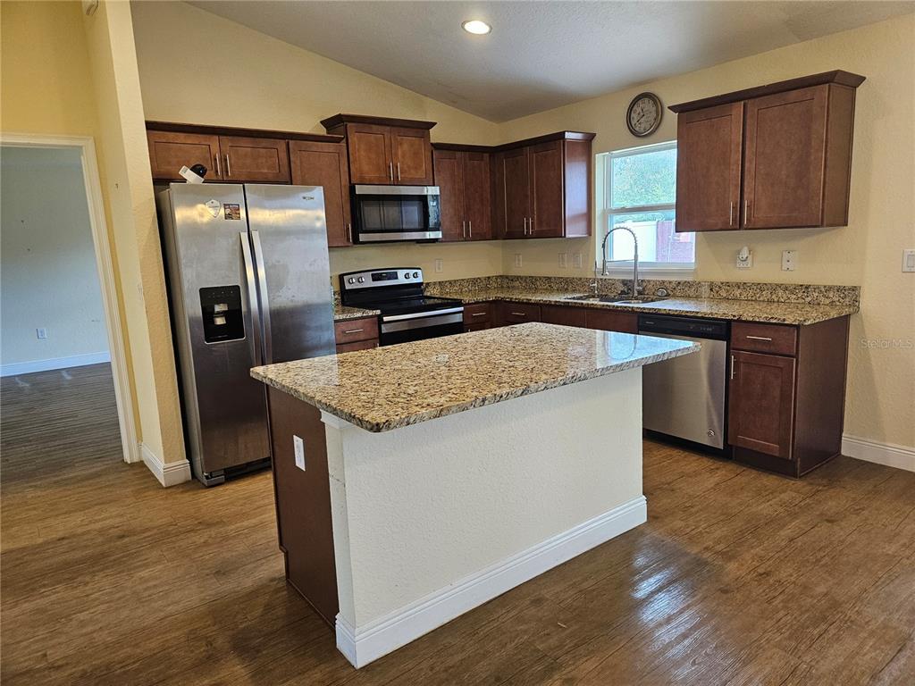 A kitchen features dark wood cabinets, granite countertops, stainless steel appliances, and a central island — 11 ALMOND TRAIL, OCALA, FL