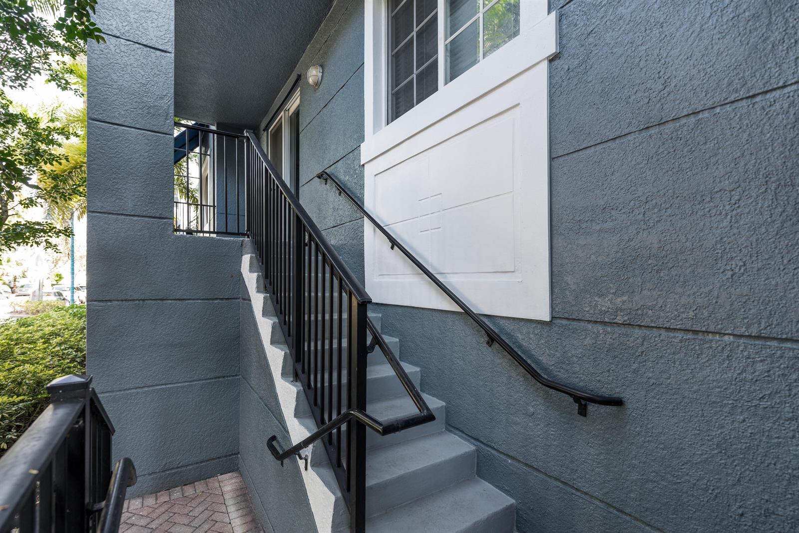 An exterior view of a gray building featuring a concrete staircase with black railings — 255 NE 3rd Avenue # 2212, Delray Beach FL 33444, DELRAY BEACH, FL