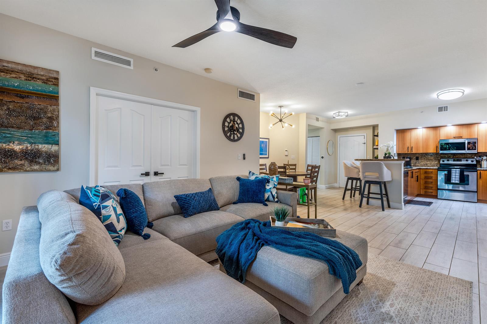 A living room with a sectional sofa opens into a kitchen with wooden cabinets — 255 NE 3rd Avenue # 2212, Delray Beach FL 33444, DELRAY BEACH, FL