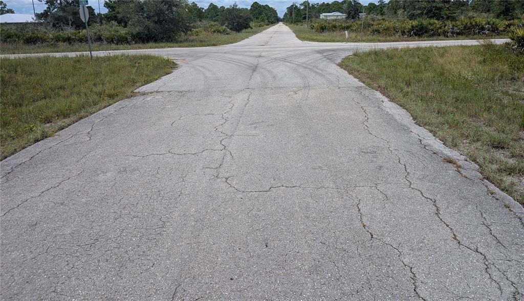 A paved road intersection surrounded by grassy fields and scattered trees under a cloudy sky — 3430 GERBER AVENUE, LAKE PLACID, FL