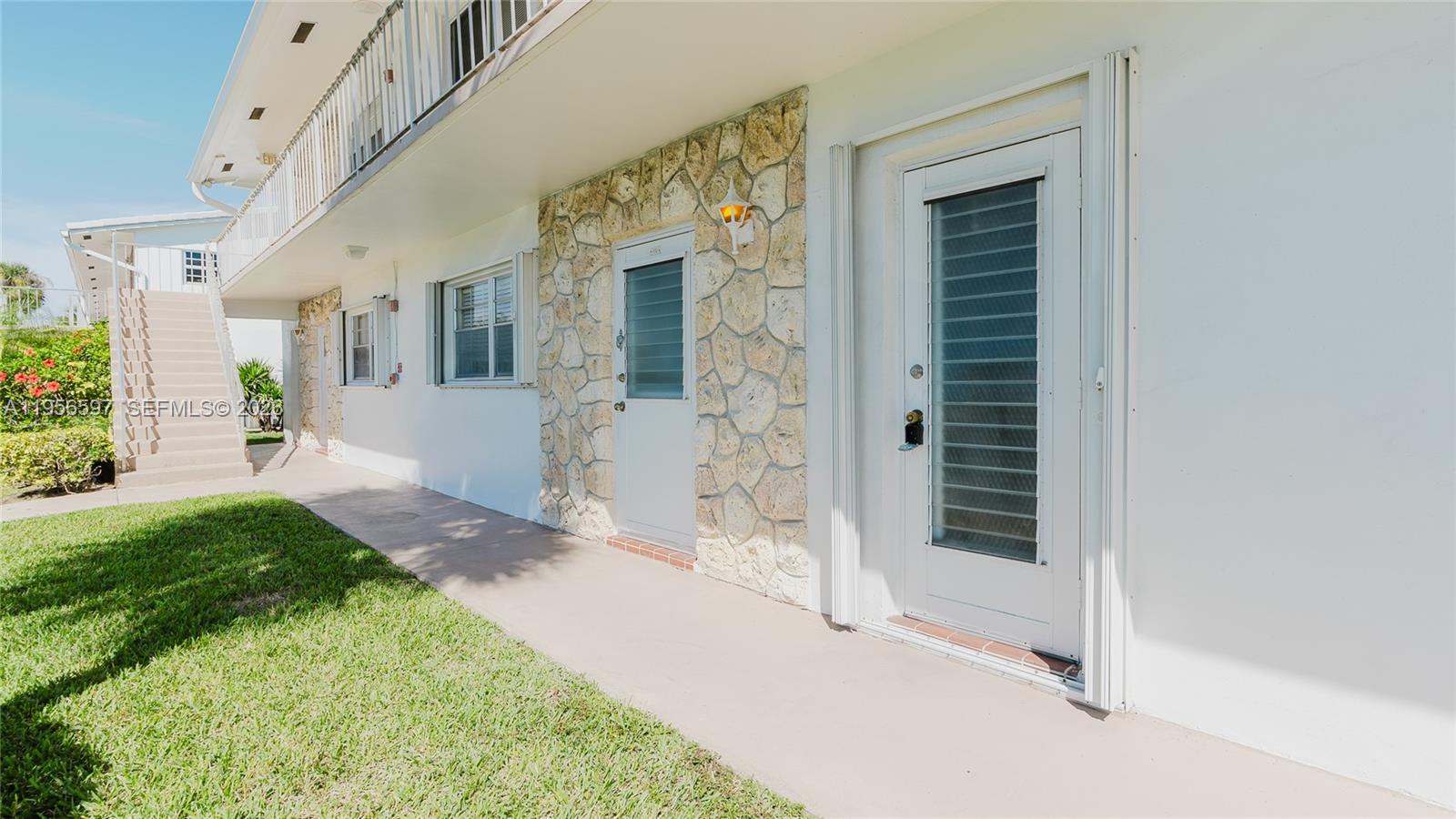 A white building exterior features a stone-accented wall, two glass-paneled doors, and a staircase — 301 S Golf Blvd # 172, Pompano Beach FL 33064, POMPANO BEACH, FL