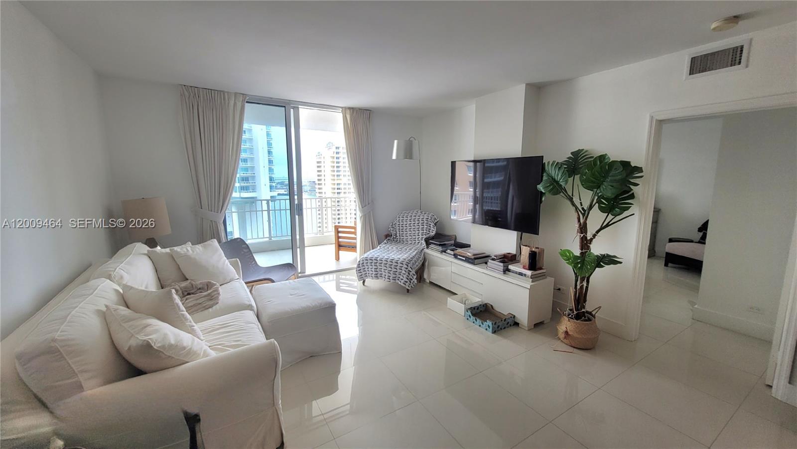 A bright living room features a white sofa, a television, and a balcony with city views — 701 Brickell Key Blvd # 2306, Miami FL 33131, MIAMI, FL