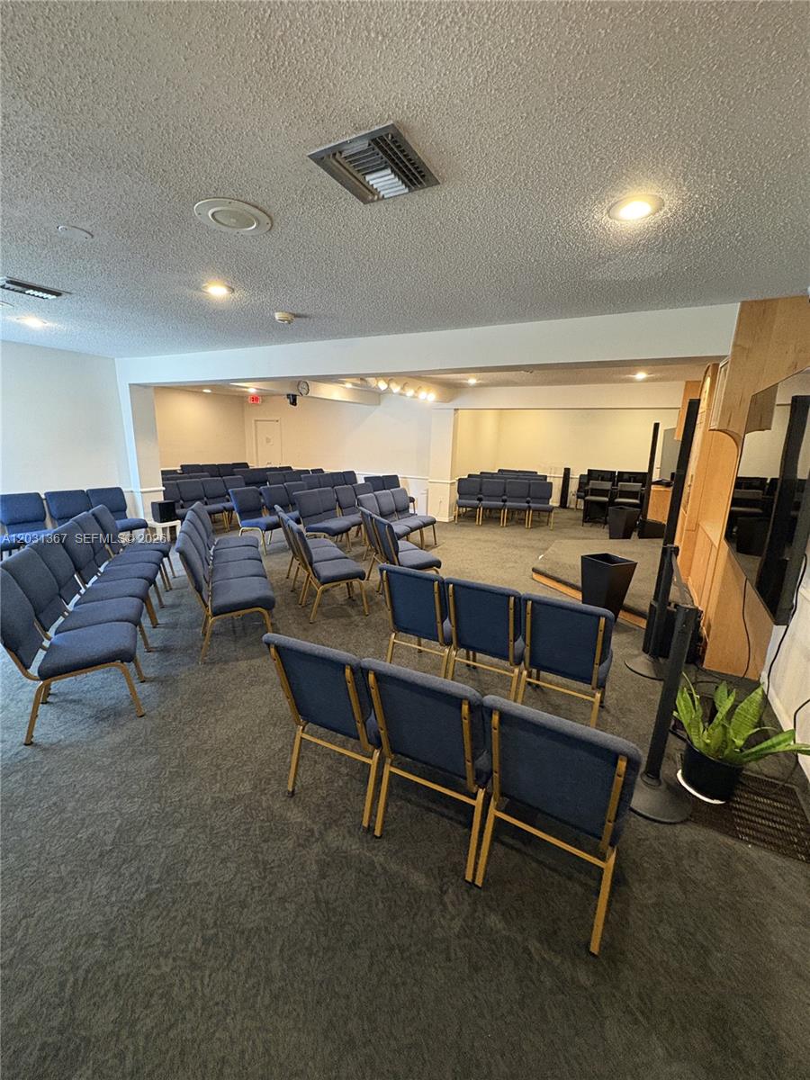 A room with rows of blue chairs, carpeted flooring, and a small stage area — 11715 SW 87th Ave, Miami FL 33176, MIAMI, FL