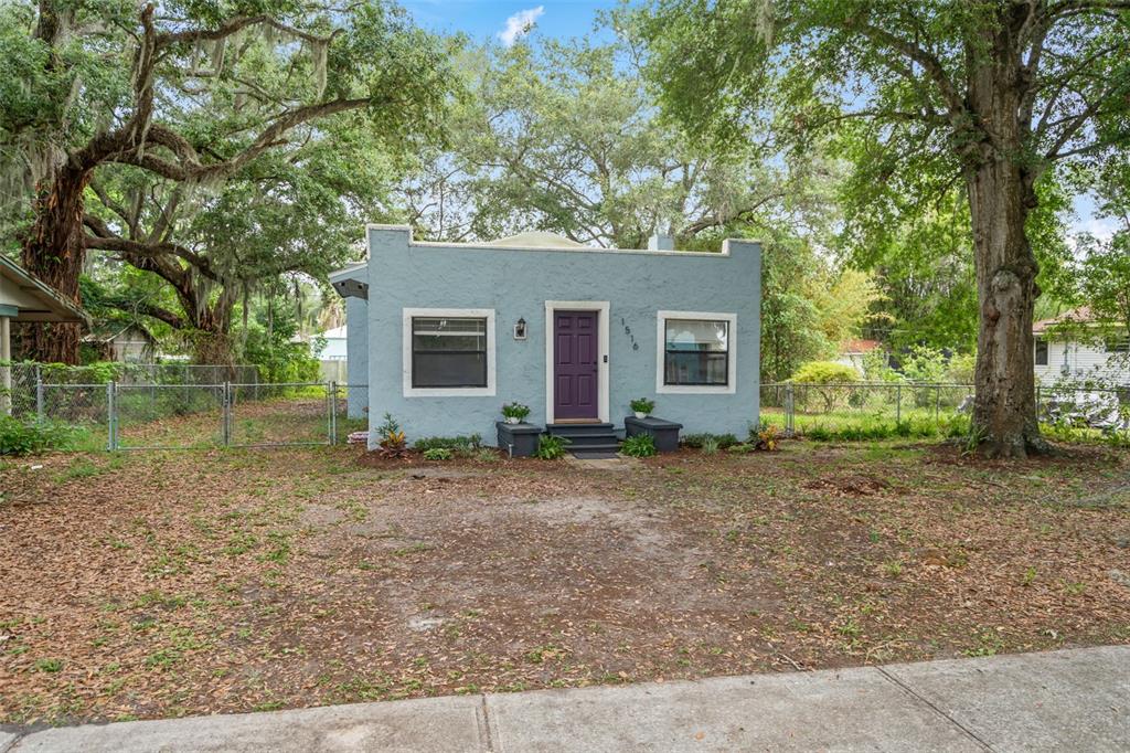A light blue, single-story stucco house with a purple front door sits behind a yard — 1516 E ELM ROAD, LAKELAND, FL
