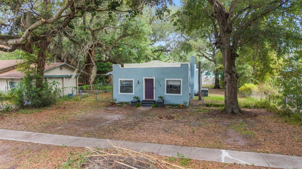 A light blue, single-story stucco house with a flat roof sits behind a chain-link fence — 1516 E ELM ROAD, LAKELAND, FL