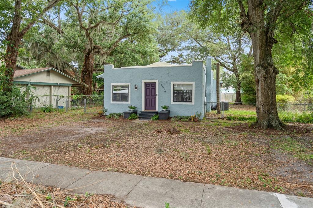 A light blue stucco house with a purple front door sits behind a dirt yard — 1516 E ELM ROAD, LAKELAND, FL