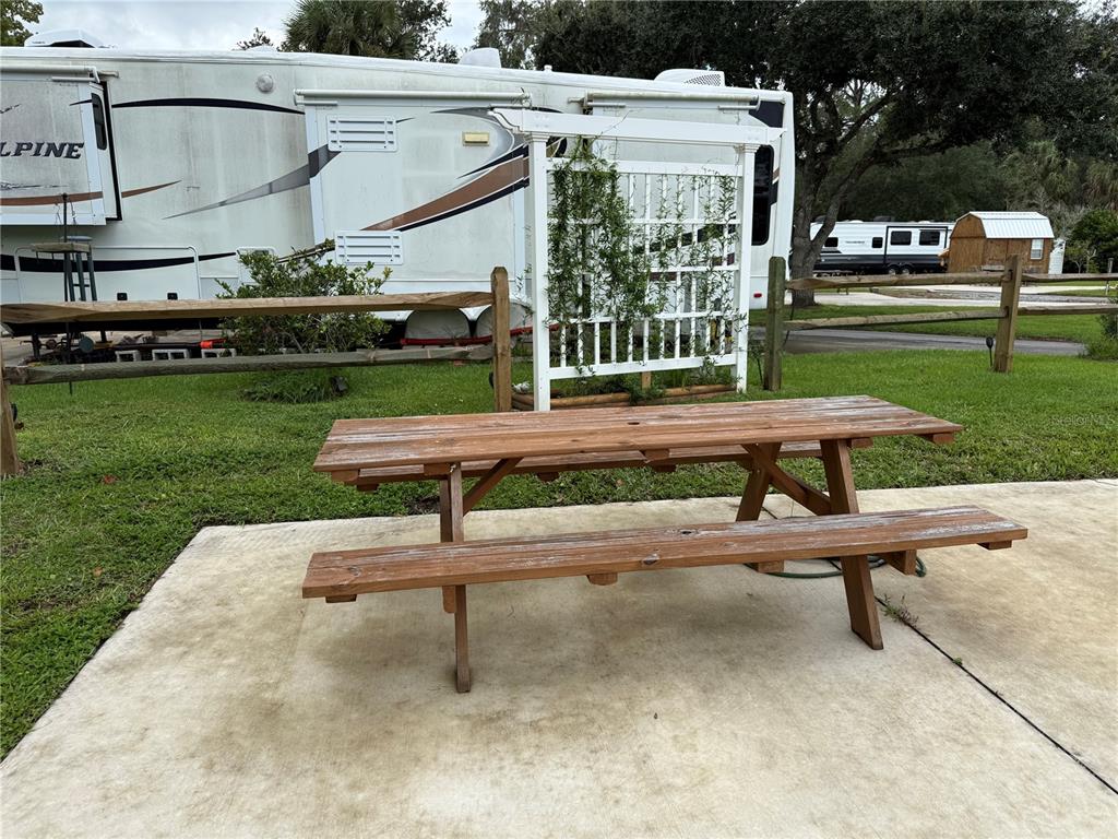 A wooden picnic table sits on a concrete patio in front of a parked RV — 2870 NE 103RD AVENUE, SILVER SPRINGS, FL