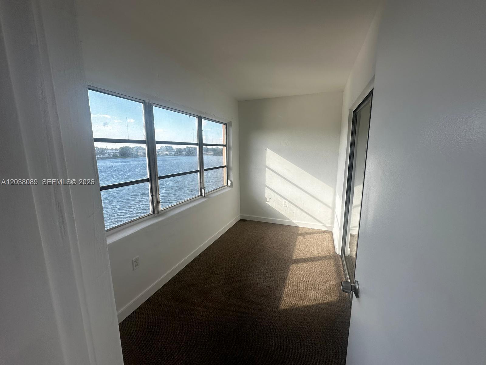 A narrow room with brown carpet, white walls, and large windows overlooking the water — 18700 NE 3rd Ct # 626, Miami FL 33179, MIAMI, FL