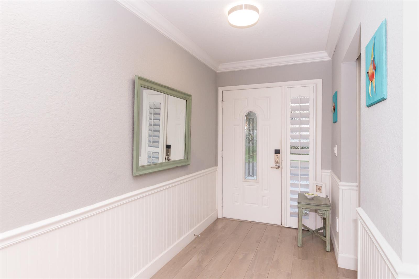 An entryway features light gray walls, white wainscoting, a white front door, and wood-look flooring — 4041 NE Breakwater Drive, Jensen Beach FL 34957, JENSEN BEACH, FL