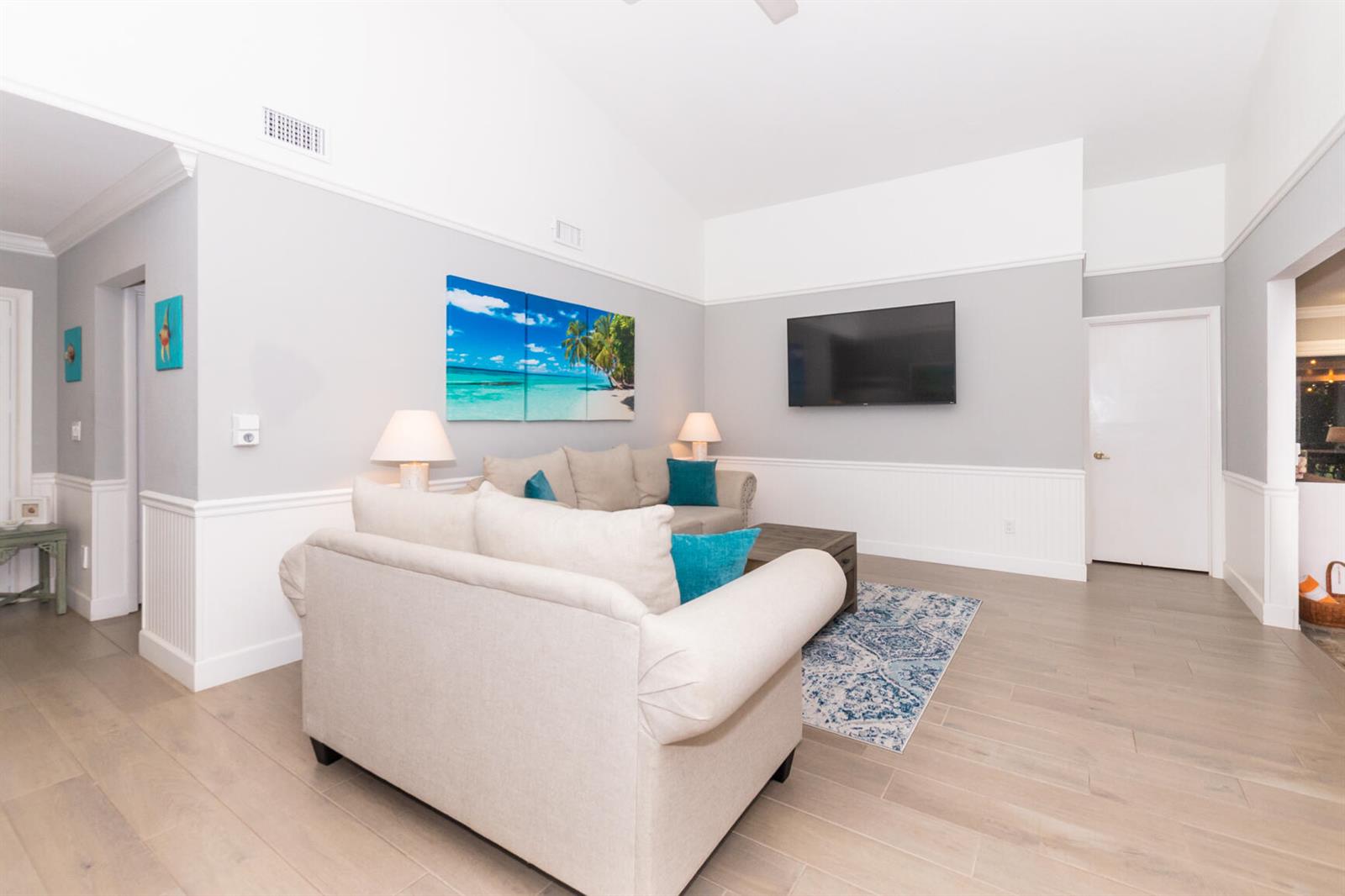 A living room features light-colored sofas, a wall-mounted television, and a blue patterned area rug — 4041 NE Breakwater Drive, Jensen Beach FL 34957, JENSEN BEACH, FL