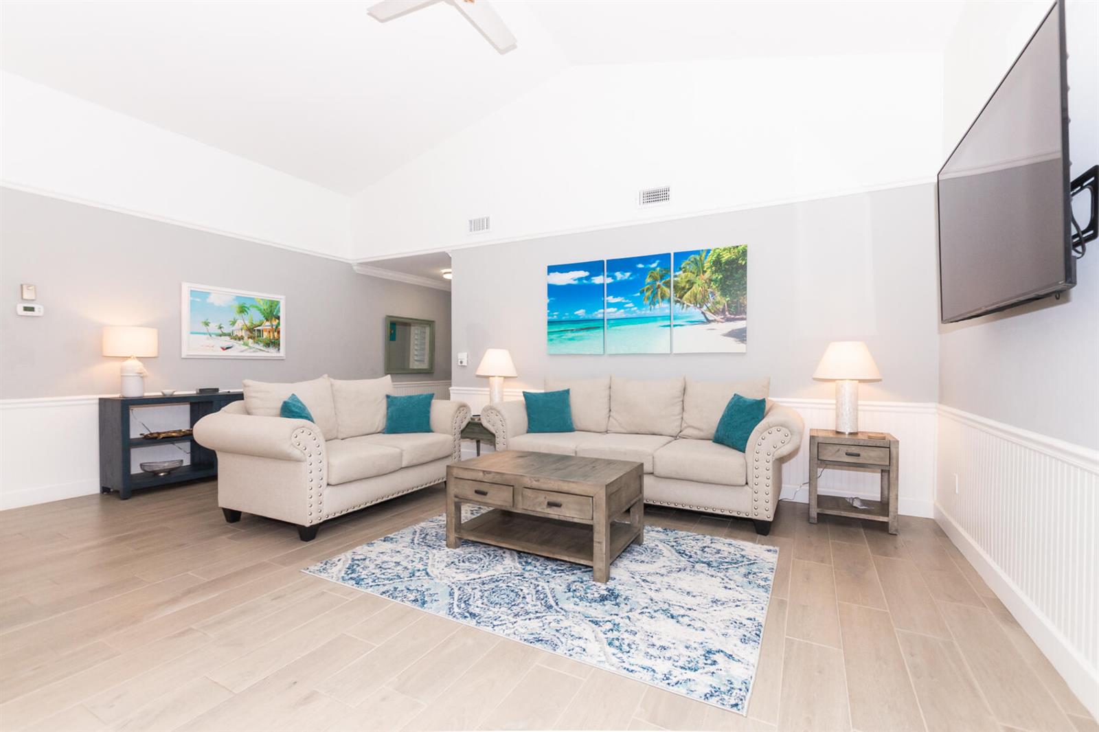 A living room features two beige sofas, a wooden coffee table, and beach-themed wall art — 4041 NE Breakwater Drive, Jensen Beach FL 34957, JENSEN BEACH, FL