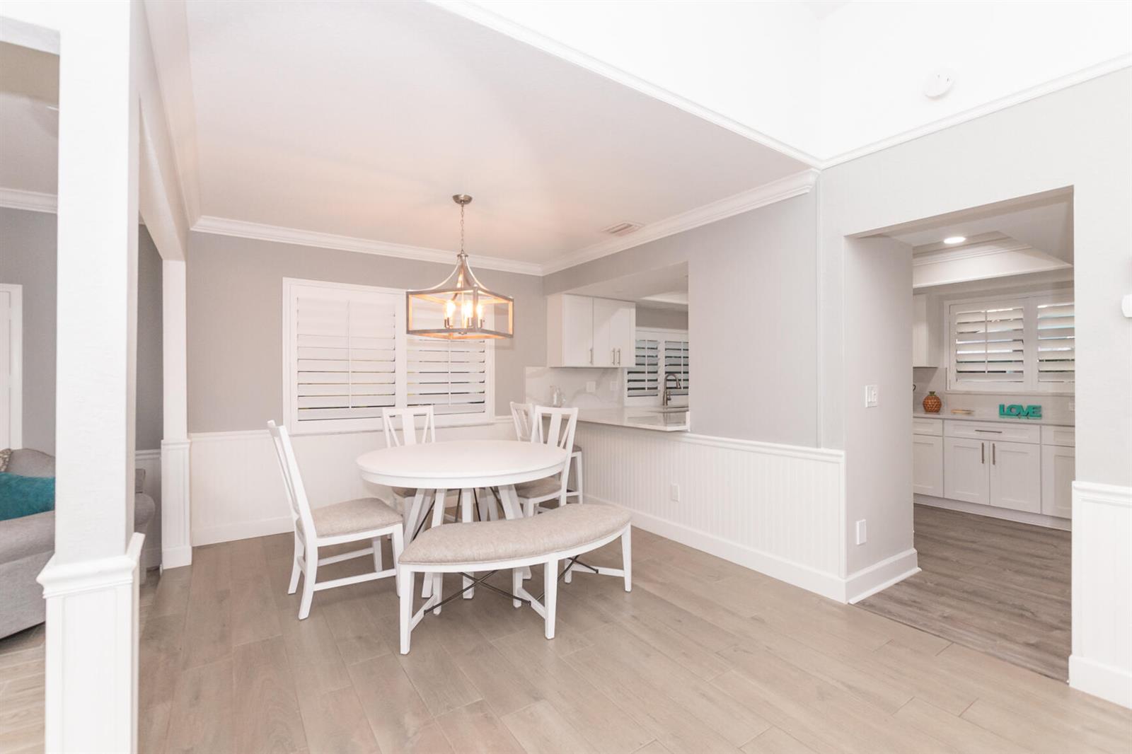 A dining area with a round white table, chairs, and bench, featuring light wood flooring — 4041 NE Breakwater Drive, Jensen Beach FL 34957, JENSEN BEACH, FL