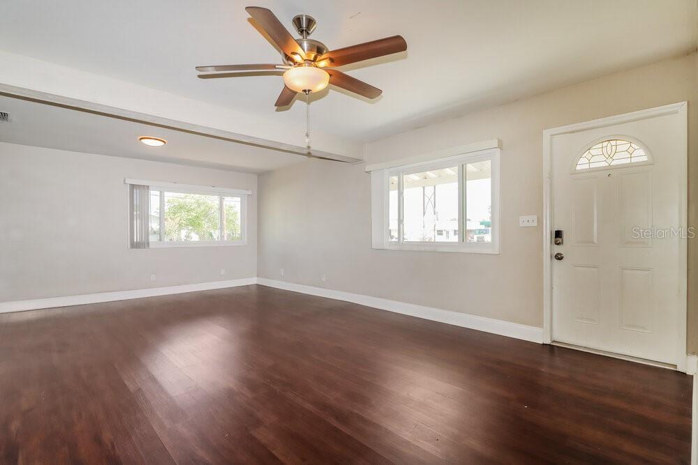 A living room with wood-look flooring, light gray walls, a ceiling fan, and a front door — 5100 98TH AVENUE N, PINELLAS PARK, FL
