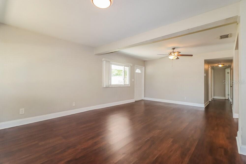 An empty living room features dark wood-look flooring, beige walls, and a ceiling fan — 5100 98TH AVENUE N, PINELLAS PARK, FL