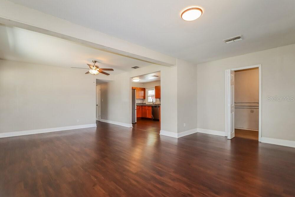 An open-concept living area features dark wood flooring, beige walls, and a view into the kitchen — 5100 98TH AVENUE N, PINELLAS PARK, FL