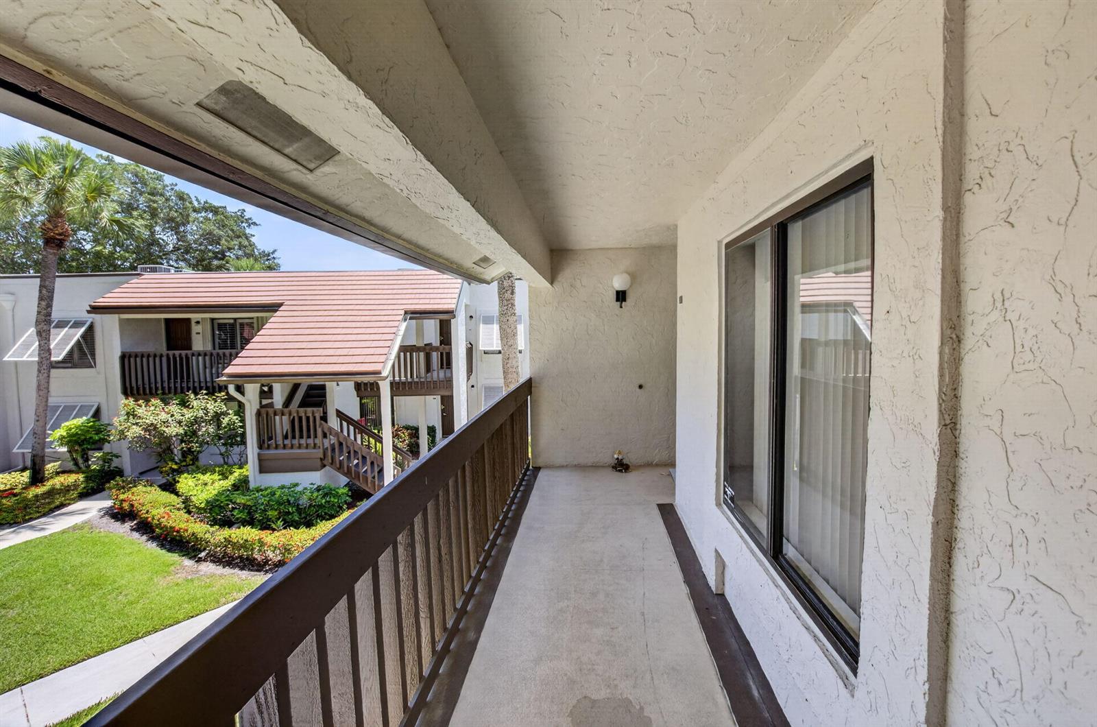 A covered balcony with a wooden railing overlooks a courtyard with a lawn and buildings — 10187 Mangrove Drive # 201, Boynton Beach FL 33437, BOYNTON BEACH, FL