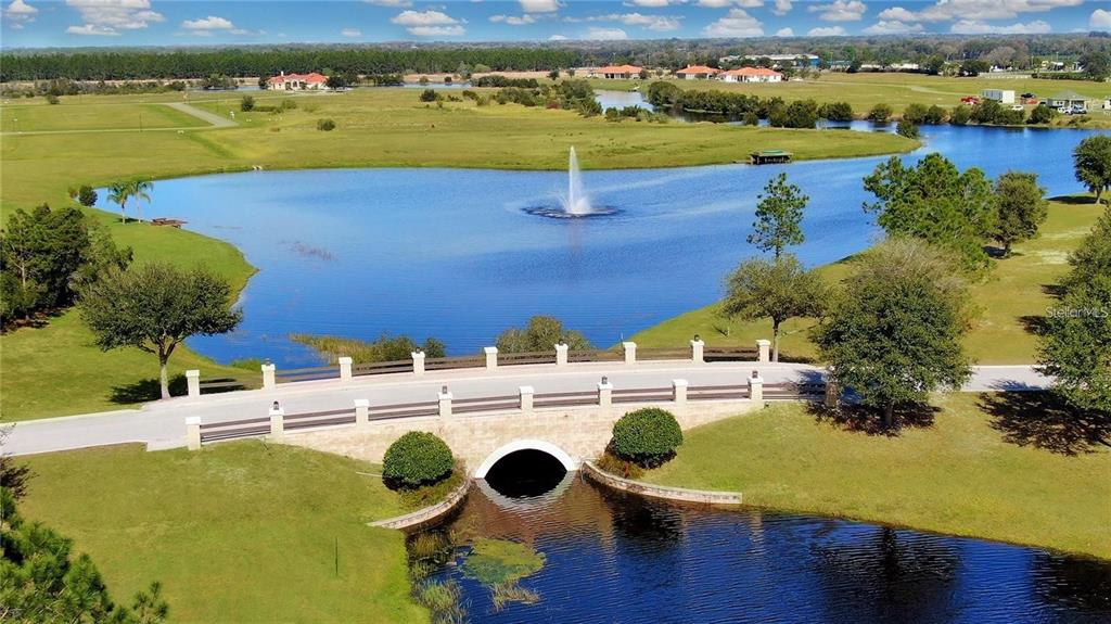 An aerial view shows a stone bridge crossing a pond with a central water fountain — 5234 LAKE VENICE DRIVE, WIMAUMA, FL