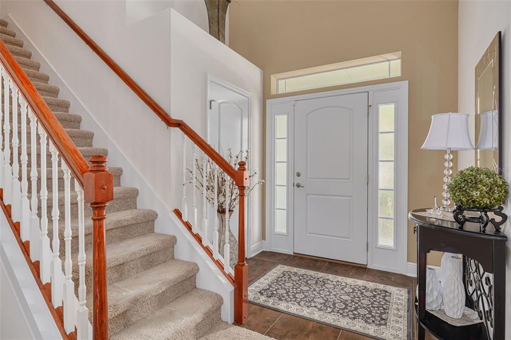 An entryway features a carpeted staircase with a wooden railing, a white front door, and tile — 20215 NATURES SPIRIT DRIVE, TAMPA, FL