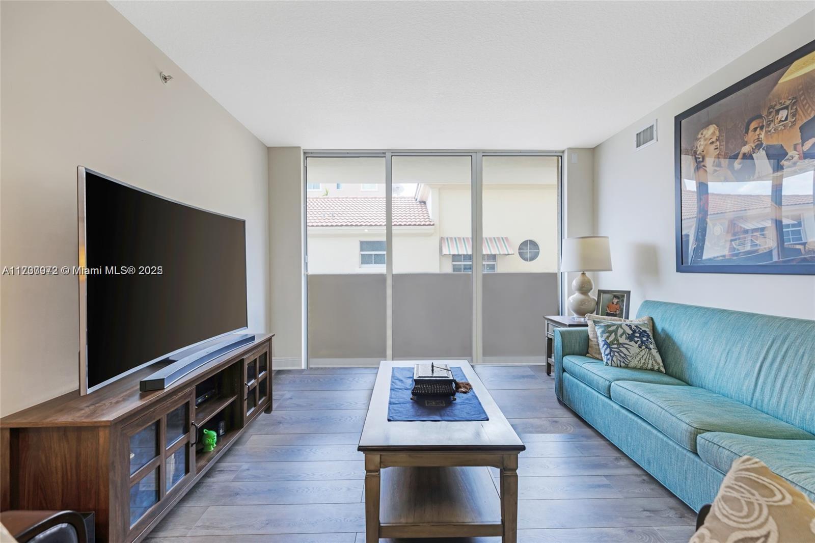 A living room features a teal sofa, a wooden media console, and a sliding glass door — 3232 SW 22nd Ter # 301, Miami FL 33145, MIAMI, FL