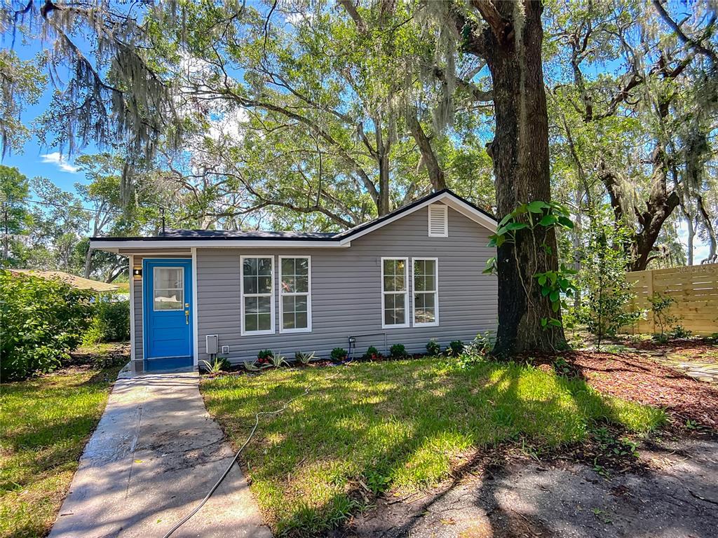 A small, gray-sided house with a bright blue door sits under large, moss-covered oak trees — 8781 S LAKESHORE DRIVE, FLORAL CITY, FL