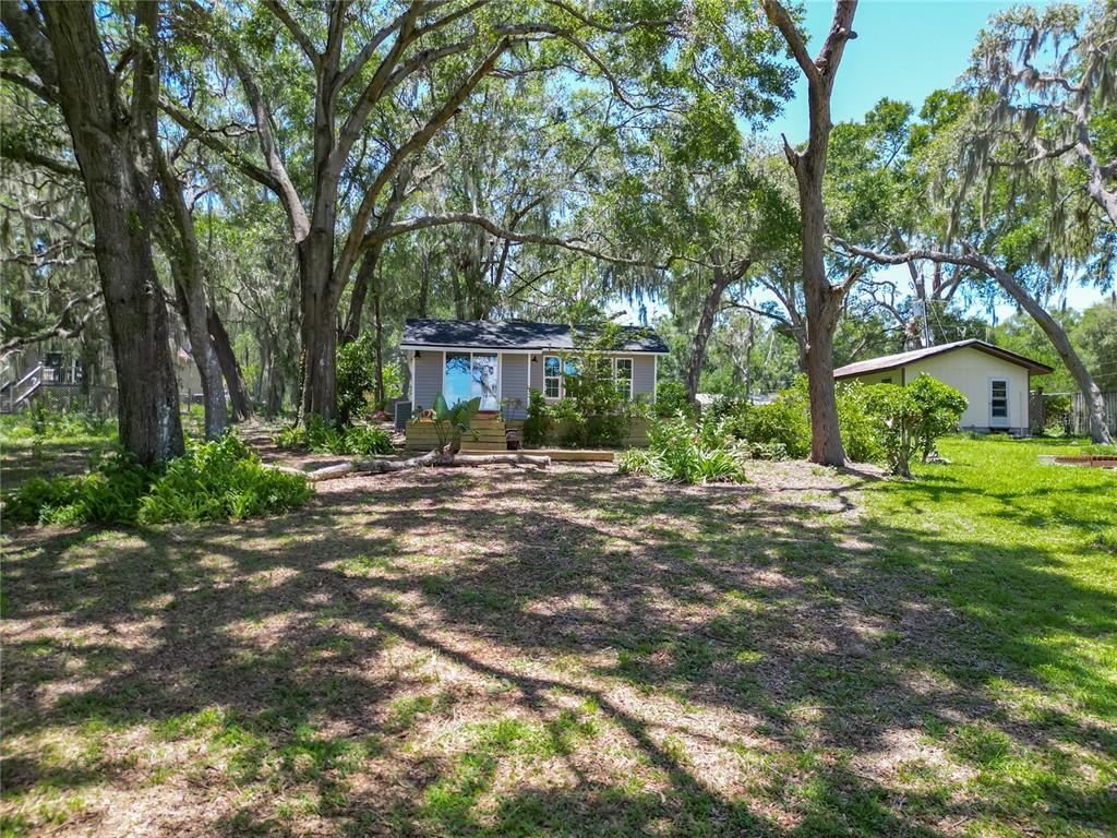 A small house with a deck stands in a yard shaded by large oak trees — 8781 S LAKESHORE DRIVE, FLORAL CITY, FL
