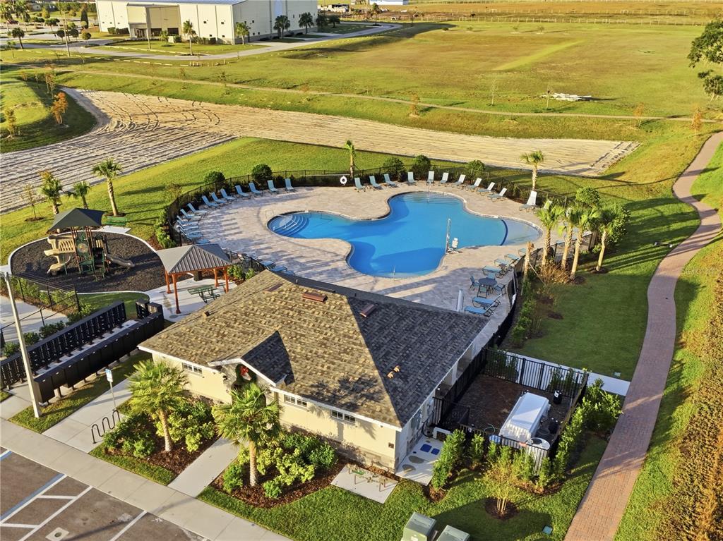 An aerial view shows a community swimming pool, playground, and clubhouse with a parking lot — 4223 HILLOCK BOULEVARD, HAINES CITY, FL