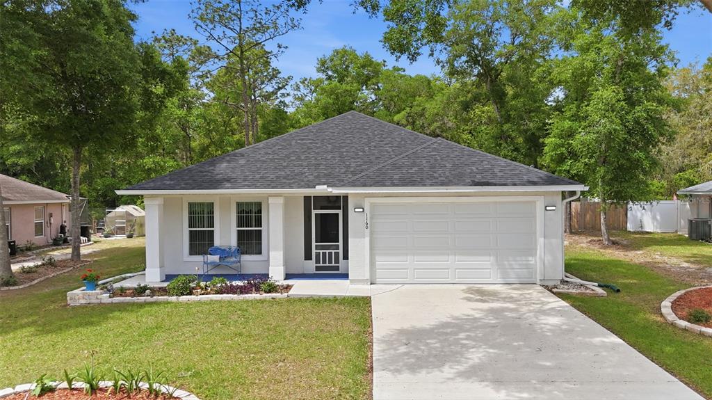 A single-story house with a white stucco exterior, dark shingled roof, and a two-car garage — 1160 NE 130TH TERRACE, SILVER SPRINGS, FL