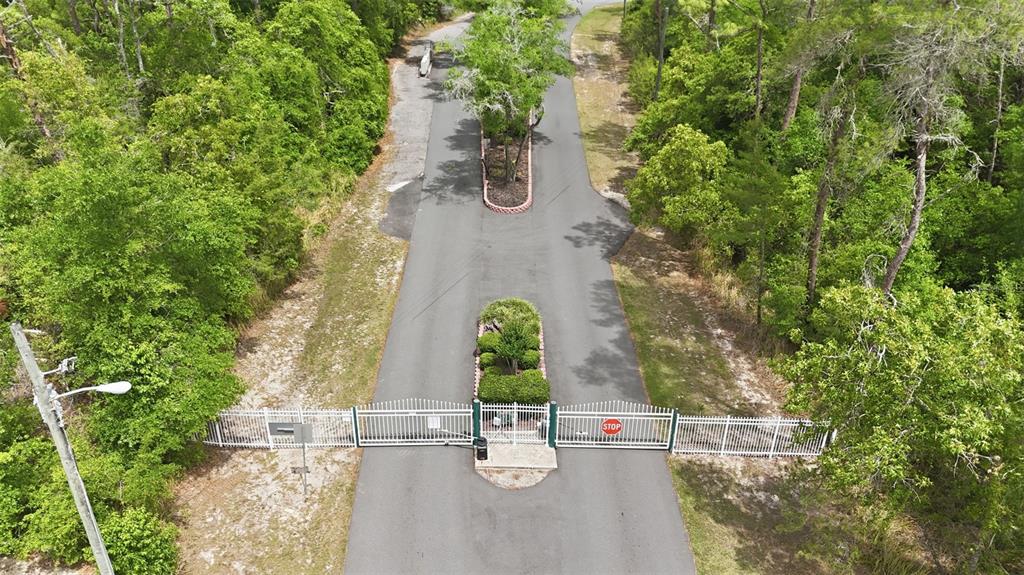 An aerial view shows a gated entrance with a central landscaped median and surrounding trees — 1160 NE 130TH TERRACE, SILVER SPRINGS, FL