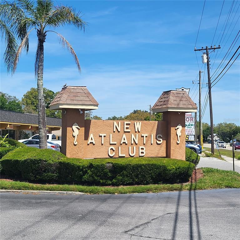 A tan monument sign for the New Atlantis Club stands in front of a parking lot — 12760 INDIAN ROCKS ROAD UNIT 306, LARGO, FL