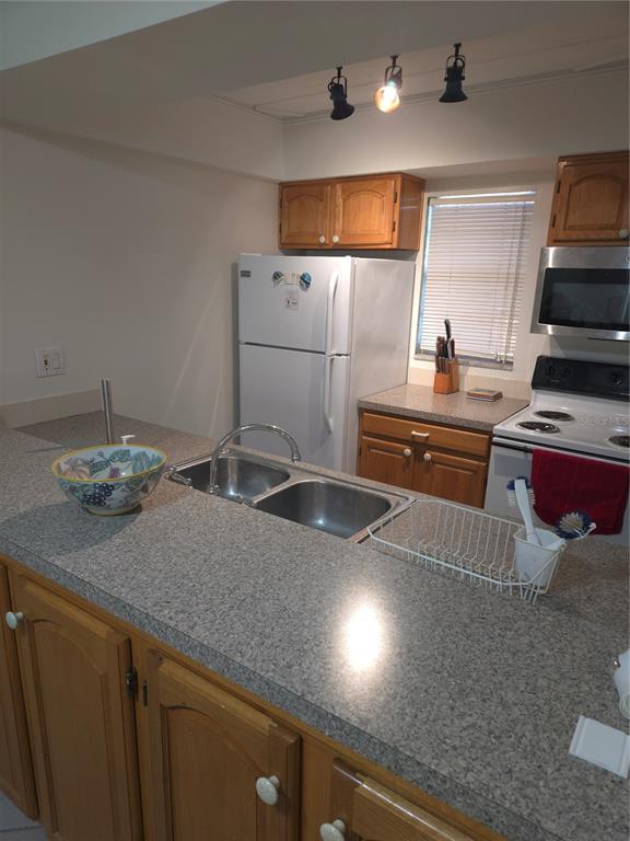 A kitchen features wood cabinets, a double sink, granite-look countertops, and white appliances — 12760 INDIAN ROCKS ROAD UNIT 306, LARGO, FL