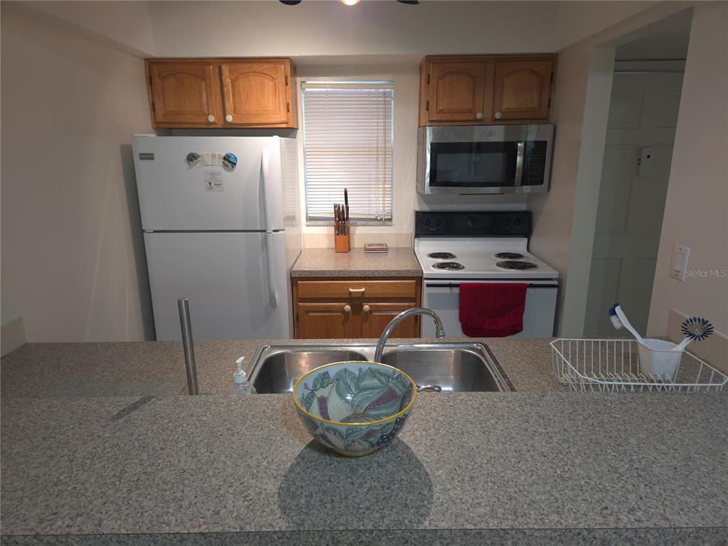 A kitchen features wood cabinets, white appliances, a double sink, and a granite-look countertop — 12760 INDIAN ROCKS ROAD UNIT 306, LARGO, FL