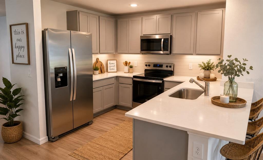 A kitchen features light gray cabinets, stainless steel appliances, and a white quartz island countertop — 230 BULL FROG LANE, UMATILLA, FL