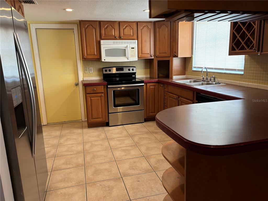 A kitchen features wood cabinets, stainless steel appliances, a tile floor, and a peninsula counter — 9616 LAKE CHRISTINA LANE, PORT RICHEY, FL