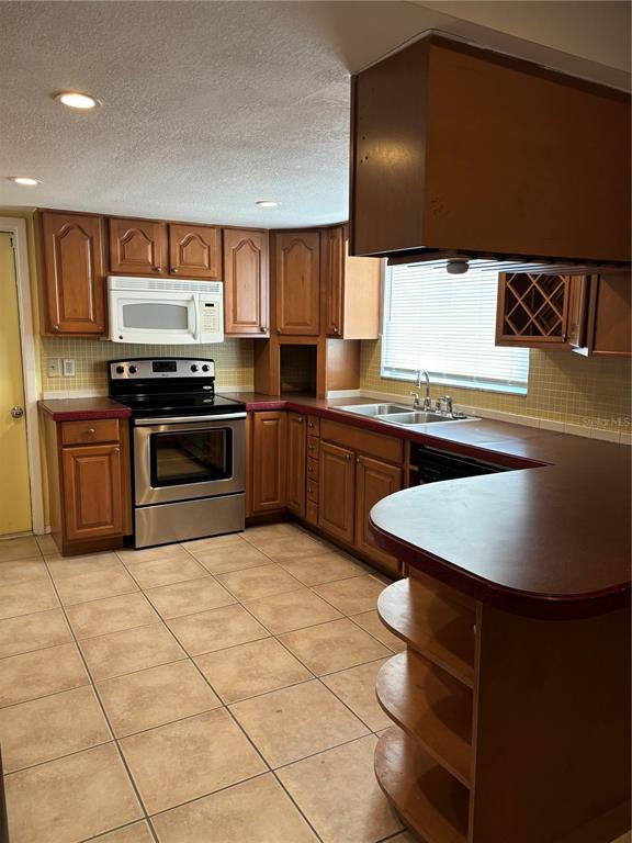 A kitchen features wood cabinets, a stainless steel stove, and a red countertop peninsula — 9616 LAKE CHRISTINA LANE, PORT RICHEY, FL