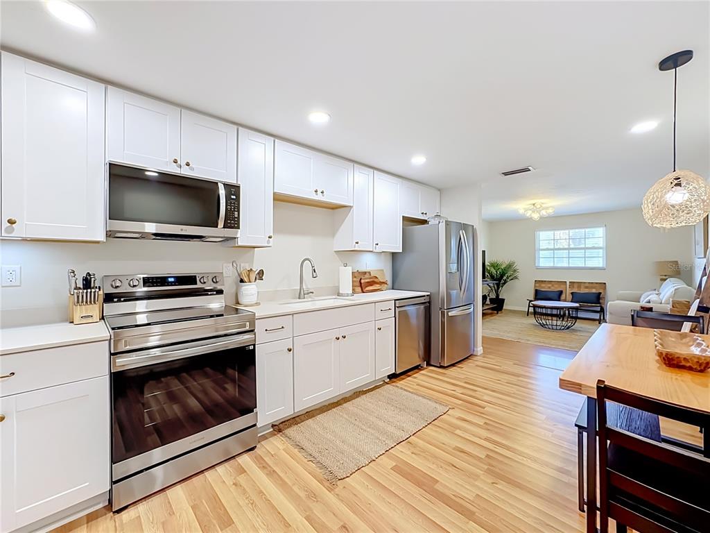 A modern kitchen with white cabinets, stainless steel appliances, and wood flooring opens to a living area — 202 PEACOCK LANE UNIT B, HOLMES BEACH, FL