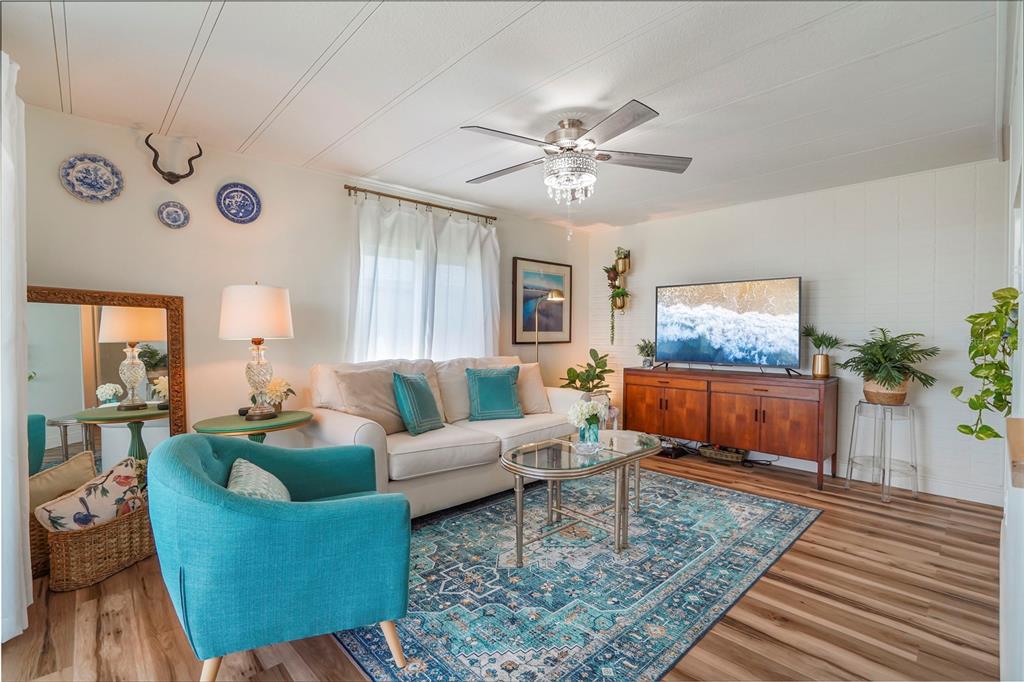 A living room features a teal armchair, a white sofa, a television, and a rug — 512 IMPERIAL DRIVE, NORTH PORT, FL
